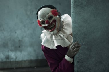 Korkunç palyaço maskesi takmış bir adam duvarın arkasına bakıyor, Cadılar Bayramı temalı.