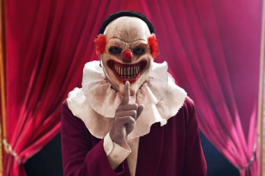 Korkunç palyaço maskesi takan bir adam sessiz hareketler yapıyor kırmızı perdeli bir parmak, Cadılar Bayramı temalı.