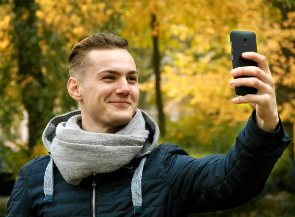 Cute young man with smartphone in autumn park