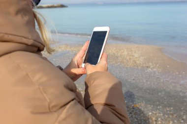 Kumsalda akıllı telefon kullanan güzel bir kadın.