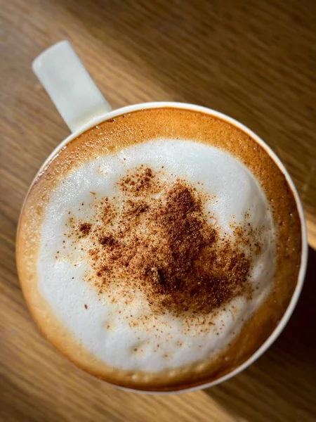 Tarçın soslu kremalı kapuçino, ahşap masada beyaz bir fincanda servis ediliyor..