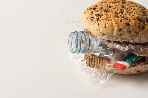 Hamburger frais savoureux avec des déchets en plastique et carton de papier à l'intérieur sur fond blanc. Les déchets recyclés dans notre concept alimentaire Image En Vente