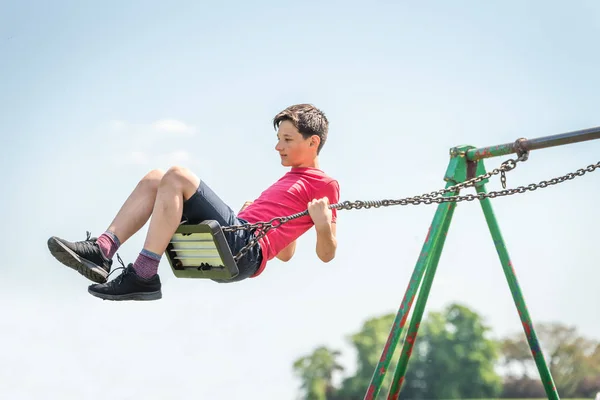 Teen chłopiec swinging wysokiej zabawy w British zabaw na jasny, słoneczny dzień — Zdjęcie stockowe