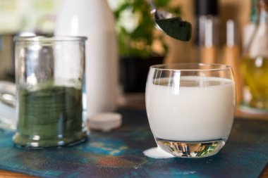 Closeup açık cam ve yeşil spirulina tozu mutfak masasının üzerinde karıştırmak hazır kaşıkla taze kefir probiotik içki görüntülemek
