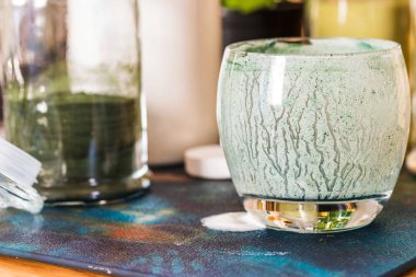 Closeup görünümü cam mutfak masasının üzerinde yeşil spirulina tozu ile karışık taze kefir probiotik içeceği boşalttı