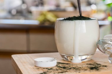 Mutfak masasının üzerinde yeşil spirulina tozu ile portre görünümü taze kefir probiotik içki açık cam içinde karışık