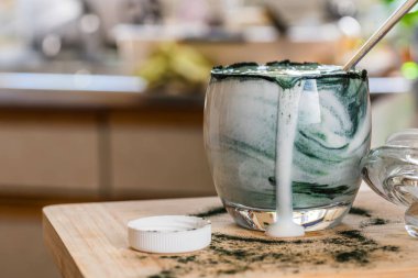 Mutfak masasının üzerinde yeşil spirulina tozu ile portre görünümü taze kefir probiotik içki açık cam içinde karışık