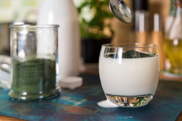 Primer plano ver kéfir fresco probiotik bebida en vidrio transparente y cuchara con espirulina verde en polvo listo para mezclar en la mesa de la cocina — Foto de Stock