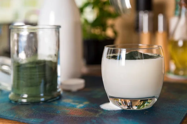 Primer plano ver kéfir fresco probiotik bebida en vidrio transparente y cuchara con espirulina verde en polvo listo para mezclar en la mesa de la cocina — Foto de Stock