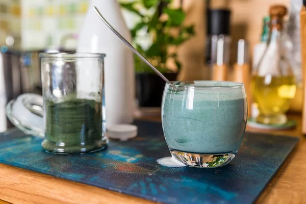 Vista close up bebida probiotik kefir fresco em vidro transparente misturado com pó espirulina verde na mesa da cozinha — Fotografia de Stock