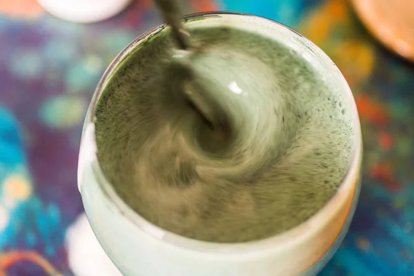 Вид крупным планом свежий кефир пробиотик напиток в прозрачном стекле смешанный с зеленой спирулиной порошок на кухонном столе — стоковое фото