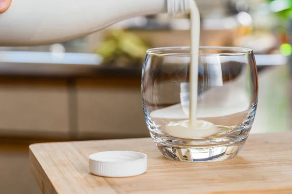 Mão derramando bebida probiotik kefir fresco de garrafa branca em vidro transparente na mesa da cozinha — Fotografia de Stock