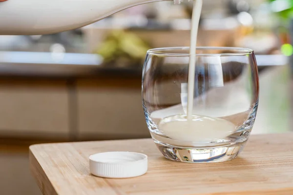 Рука наливает свежий кефировый пробиотик из белой бутылки в прозрачное стекло на кухонный стол — стоковое фото
