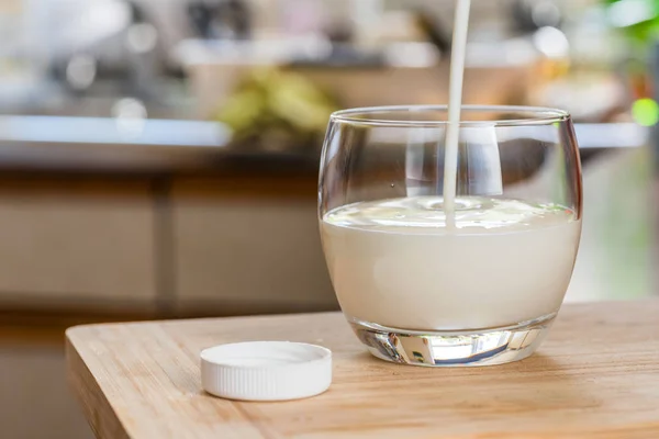 Mão derramando bebida probiotik kefir fresco de garrafa branca em vidro transparente na mesa da cozinha — Fotografia de Stock