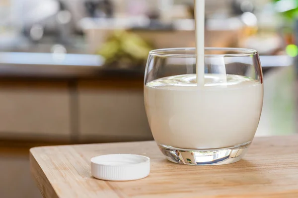 Mão derramando bebida probiotik kefir fresco de garrafa branca em vidro transparente na mesa da cozinha — Fotografia de Stock