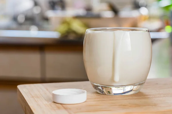 Mão derramando bebida probiotik kefir fresco de garrafa branca em vidro transparente na mesa da cozinha — Fotografia de Stock