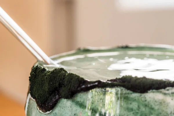 Вид крупным планом свежий кефир пробиотик напиток в прозрачном стекле смешанный с зеленой спирулиной порошок на кухонном столе — стоковое фото