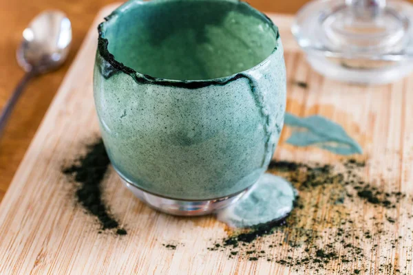 Closeup görünümü cam mutfak masasının üzerinde ahşap tahta üzerinde yeşil spirulina tozu ile karışık taze kefir probiotik içeceği boşalttı