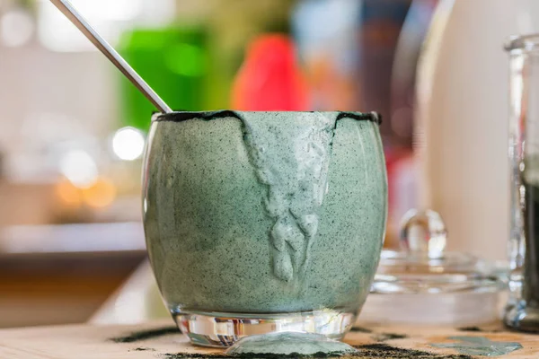 Closeup görünümü cam mutfak masasının üzerinde ahşap tahta üzerinde yeşil spirulina tozu ile karışık taze kefir probiotik içeceği boşalttı