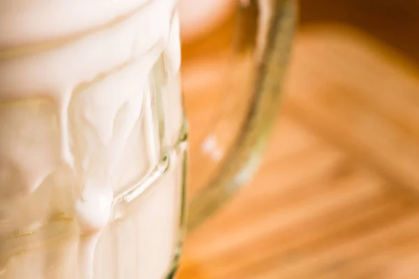Вид крупным планом свежий кефир пробиотик напиток появился из переполненного пустого стекла на кухонном столе — стоковое фото