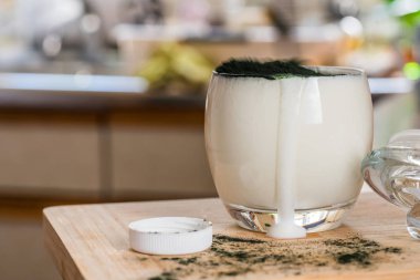 Mutfak masasının üzerinde yeşil spirulina tozu ile portre görünümü taze kefir probiotik içki açık cam içinde karışık