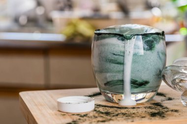 Mutfak masasının üzerinde yeşil spirulina tozu ile portre görünümü taze kefir probiotik içki açık cam içinde karışık