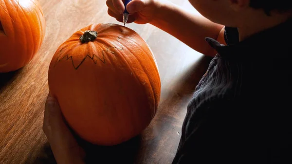 Young boy carving and painting a pumpkin for Halloween on a table — Stock Photo, Image