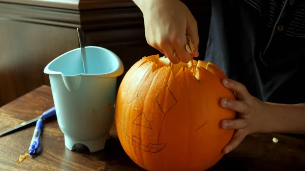 Young boy carving and painting a pumpkin for Halloween on a table — Stock Photo, Image