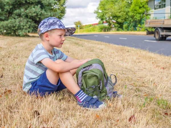 Dag bekijken kleine kind jongen reiziger met rugzak zitten naast Uk weg — Stockfoto