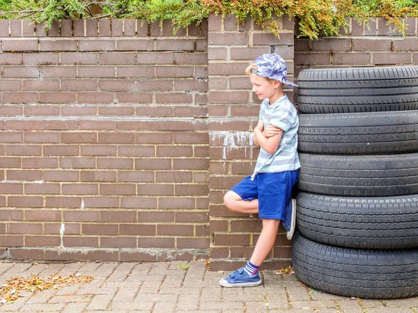 Dag weergave schattig kindje jongen poseren naast de stapel van gebruikte banden over Engelse muur — Stockfoto
