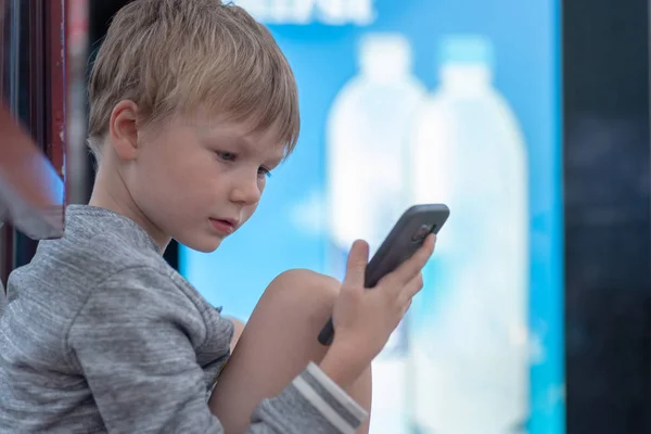 Blonde jongen met smartphone bij de bushalte in Verenigd Koninkrijk — Stockfoto