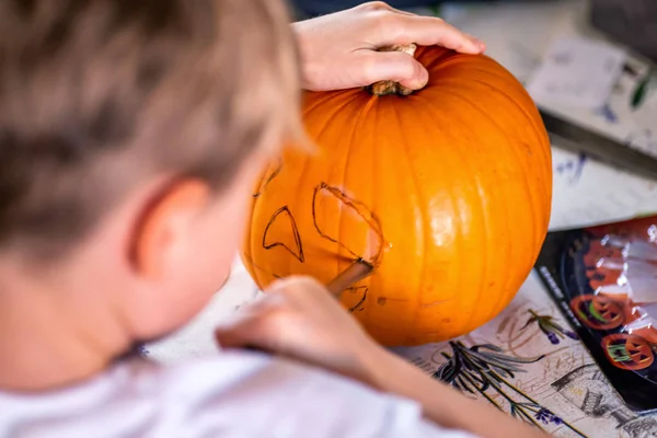 Blond boy carving pumpkin jack-o-lantern with knife — Stock Photo, Image