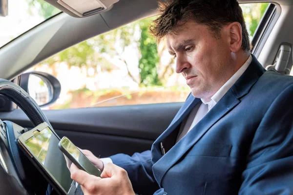 Empresario que trabaja en la tableta y el teléfono inteligente dentro del coche en el día brillante — Foto de Stock