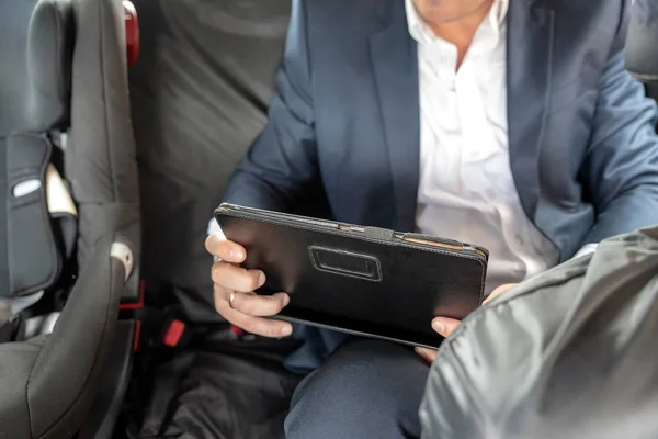 Empresario que trabaja en la tableta y el teléfono inteligente dentro del coche al lado de la silla de coche del bebé en día brillante — Foto de Stock