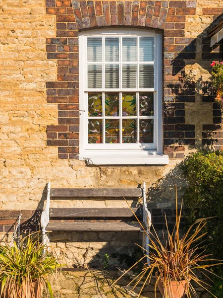 Giornata di sole vista della vecchia finestra bianca sul vecchio muro di mattoni e panchina in Inghilterra — Foto Stock