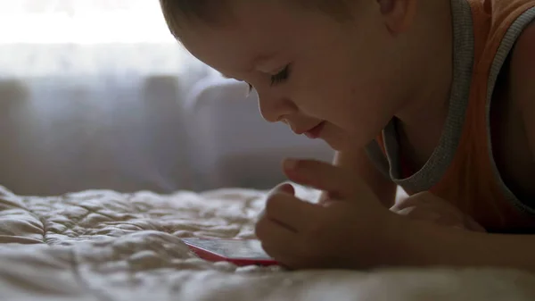 Niño niño ver jugar smartphone en la cama en casa. educación a distancia —  Fotos de Stock