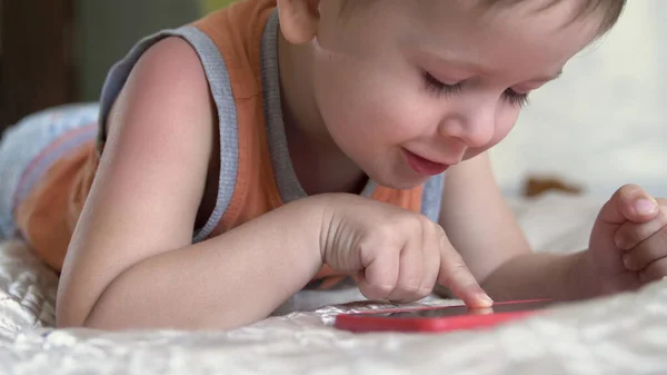 Ребенок мальчик смотреть играть смартфон на кровати дома. дистанционное обучение — стоковое фото