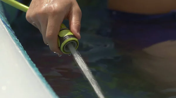 Mano adolescente riempiendo piscina gonfiabile con acqua dal tubo in giardino nel Regno Unito — Foto Stock