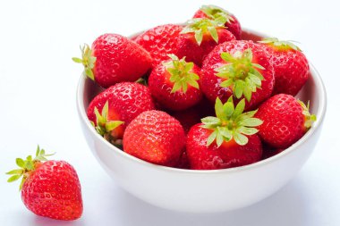 Kırsal beyaz ahşap arka planda seramik kasede taze çilek yığını.