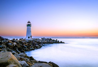 Sahilde, batan güneşin arka planında duran güzel deniz feneri.