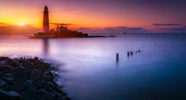 Sahilde, batan güneşin arka planında duran güzel deniz feneri.