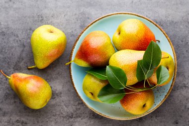 Tabağında yapraklar olan taze bir armut. Gri taş masa.