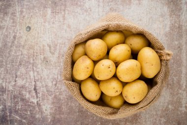Ahşap arka planda taze çiğ patates çuvalı..