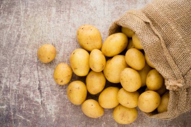 Ahşap arka planda taze çiğ patates çuvalı..