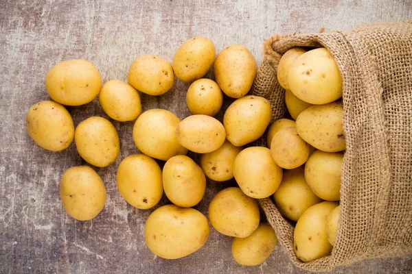 Ahşap arka planda taze çiğ patates çuvalı..