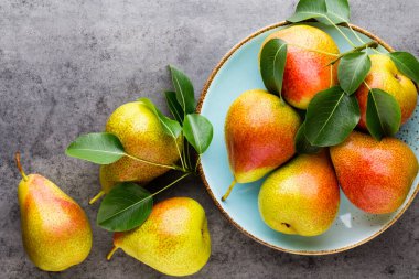 Tabağında yapraklar olan taze bir armut. Gri taş masa.