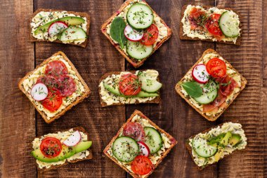 Krem peynirli, sebzeli ve salamlı mini sandviçler. Salatalıklı sandviçler, turp, domates, gri arka planda salam, üst manzara. Düz yatıyordu.