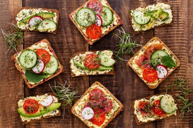 Krem peynirli, sebzeli ve salamlı mini sandviçler. Salatalıklı sandviçler, turp, domates, gri arka planda salam, üst manzara. Düz yatıyordu.