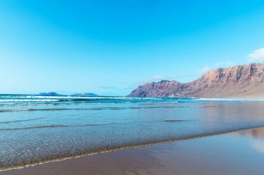 Güzel sahil manzarası ve tropikal Lanzarote denizi. Kanaryalar. Famara Sahili, Lanzarote Adası, Kanarya Adaları. Lanzarote adasındaki en popüler plajda turistler.