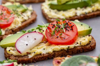 Krem peynirli, sebzeli ve salamlı mini sandviçler. Salatalıklı sandviçler, turp, domates, gri arka planda salam, üst manzara. Düz yatıyordu.